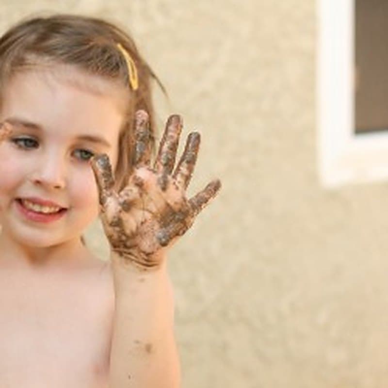 A smiling girl waving, her hands covered in paint